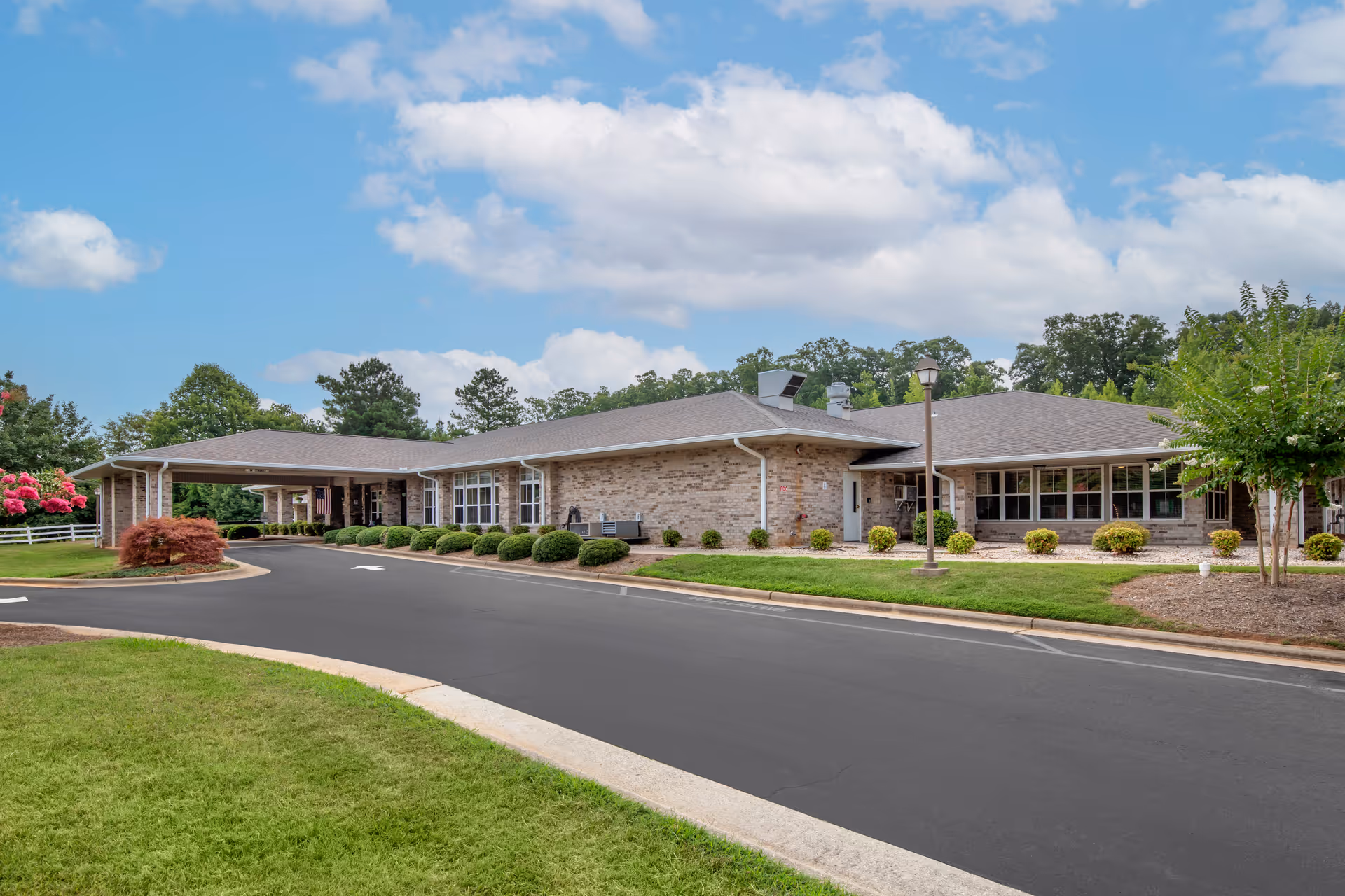 Single-story brick building with a covered entrance, circular driveway, and landscaped grounds under a blue sky.