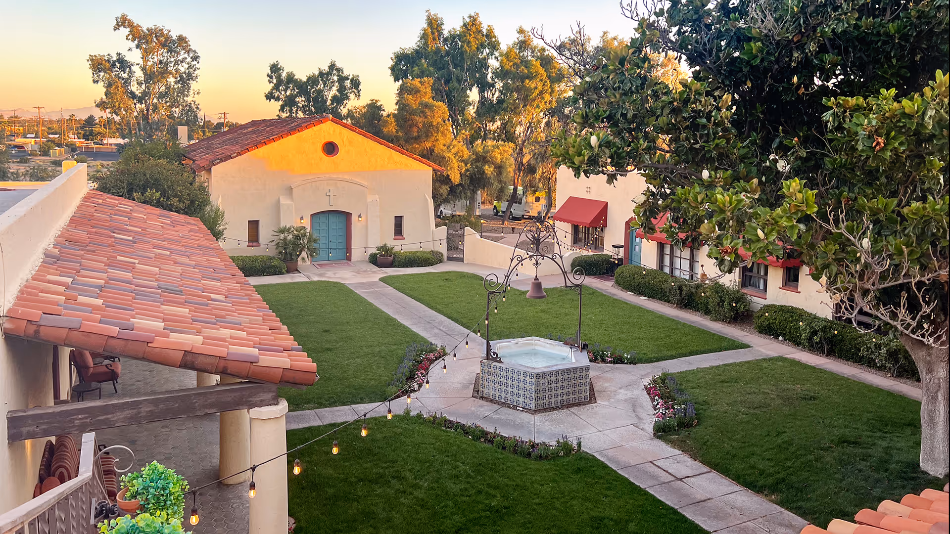 Spanish-style courtyard with a tiled central fountain, green lawns and surrounding buildings with red-tiled roofs and trees.