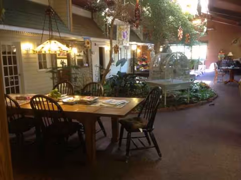 Indoor dining area at Rosemore Village with a wooden table, chairs, magazines, and garden decor.