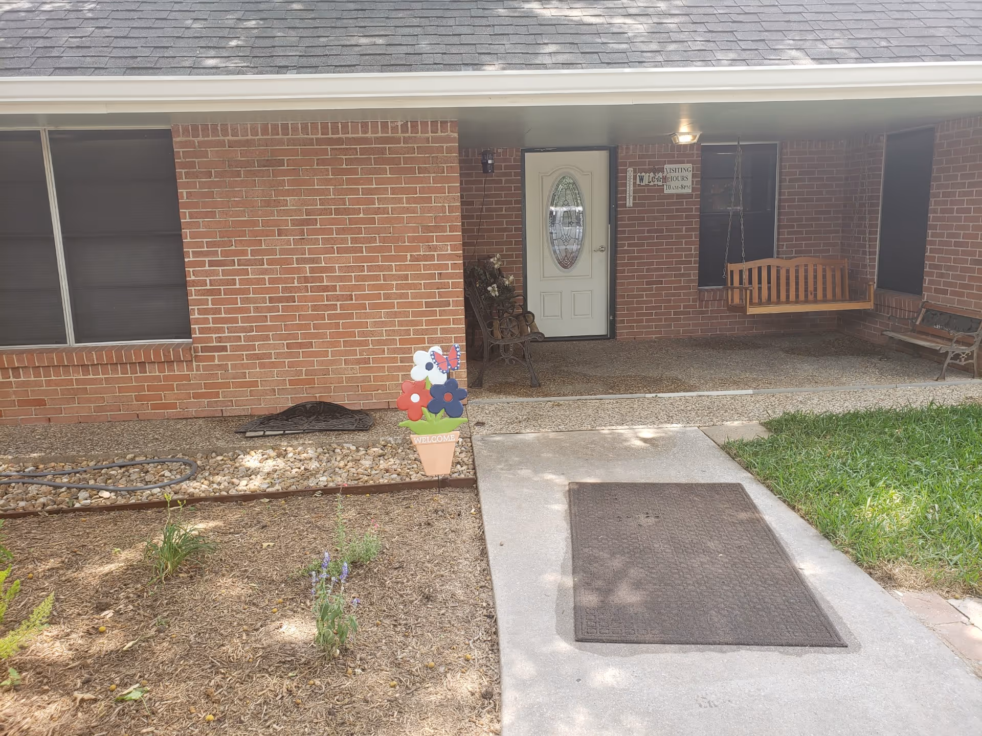 Brick facility exterior with front door, porch swing, window, and landscaping.