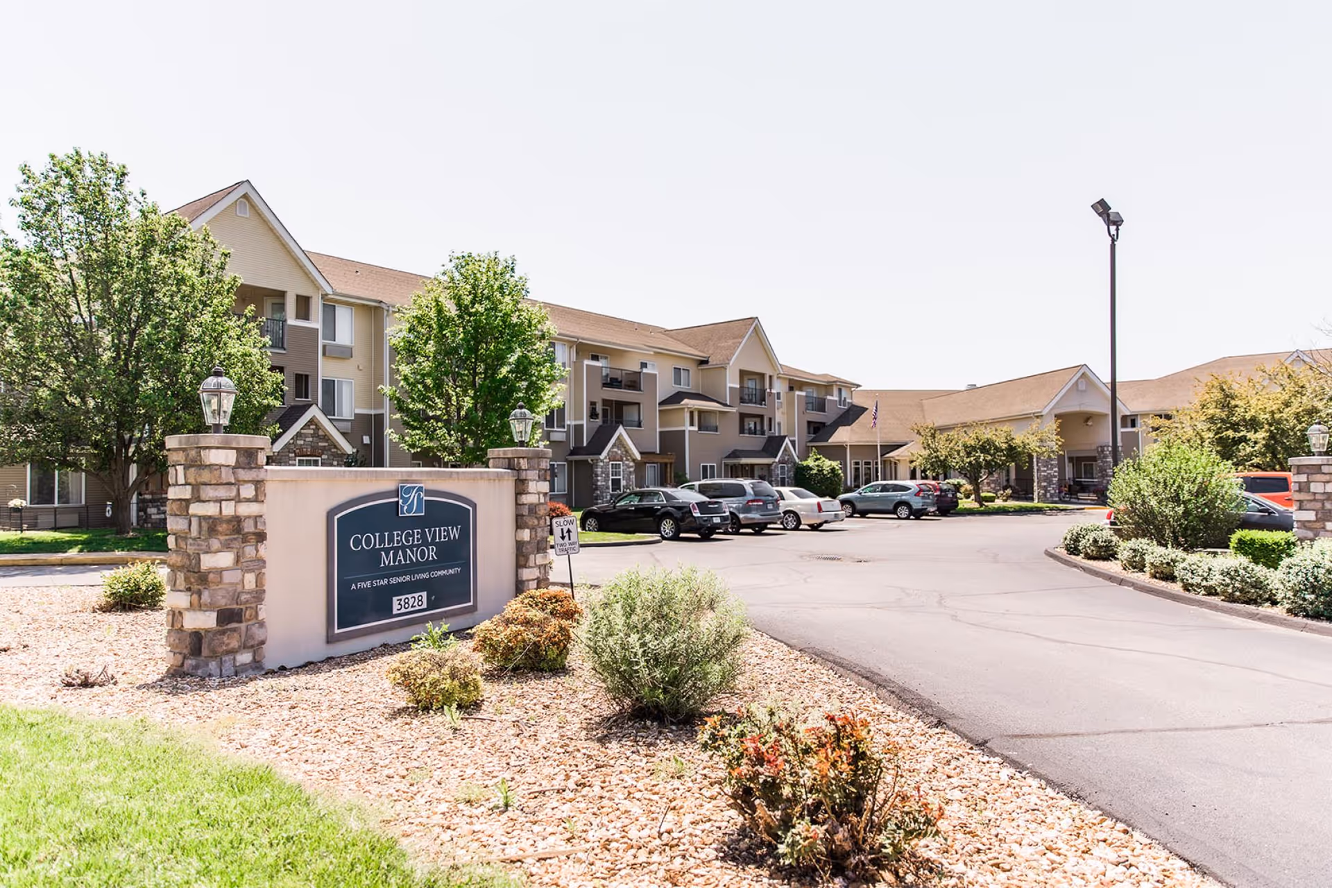 Front entrance and parking area of College View Manor senior living community with a stone name sign and landscaped driveway.
