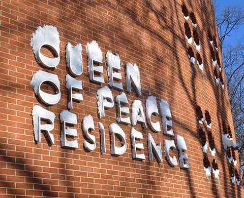 Brick facade with metal letters spelling Queen of Peace Residence.