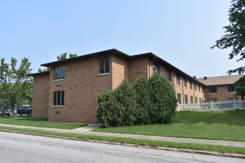 Brick, two-story senior living facility exterior with lawn, trees, and street view.