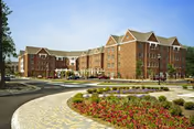 Exterior view of a large, multi-story brick senior living facility with a curved driveway and landscaped garden beds featuring flowers and shrubs in the foreground under a clear blue sky.