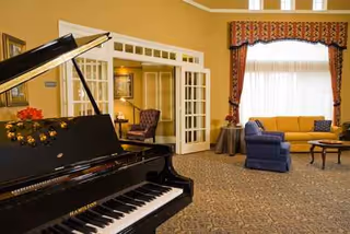 A grand piano sits in a warm living room with yellow sofa and blue chairs.