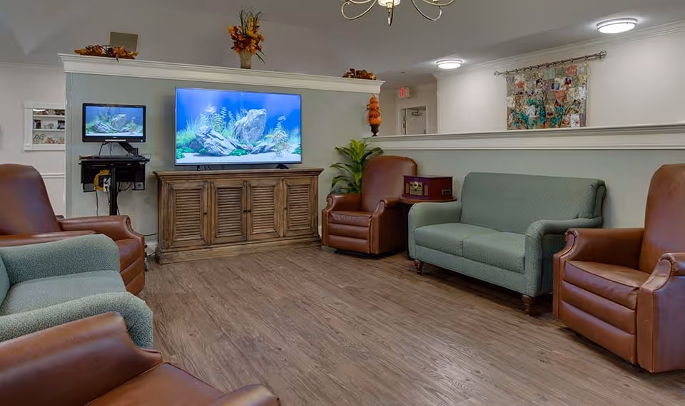 Communal living room with sofas and leather armchairs facing a large TV on a wooden cabinet.