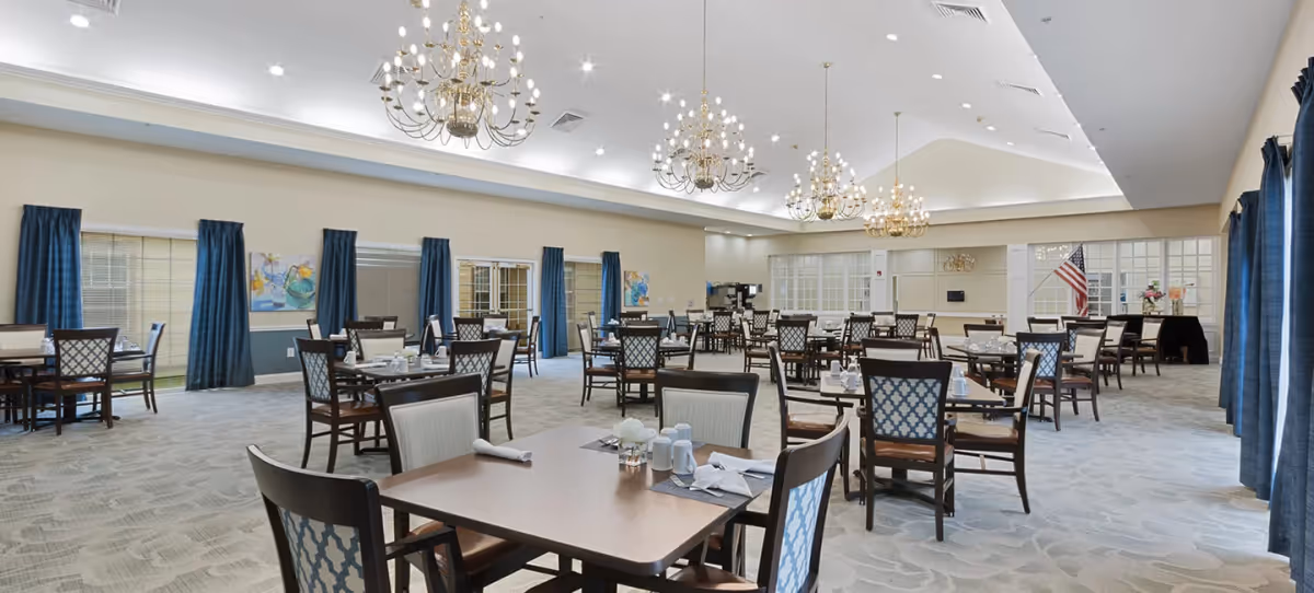 Spacious dining room with multiple set tables and chairs, chandeliers, and blue curtains.
