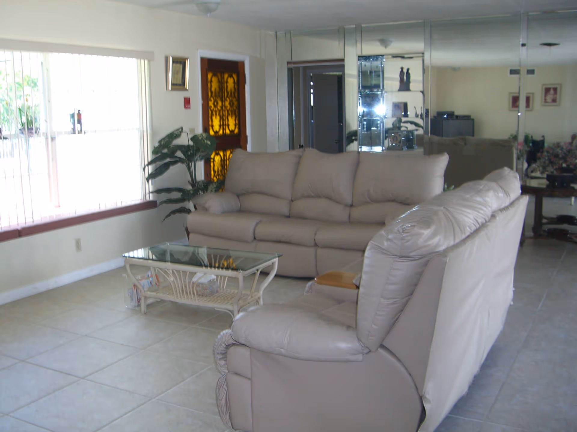 Bright living room with beige leather sofas, a glass-top coffee table, large window and mirrored wall.