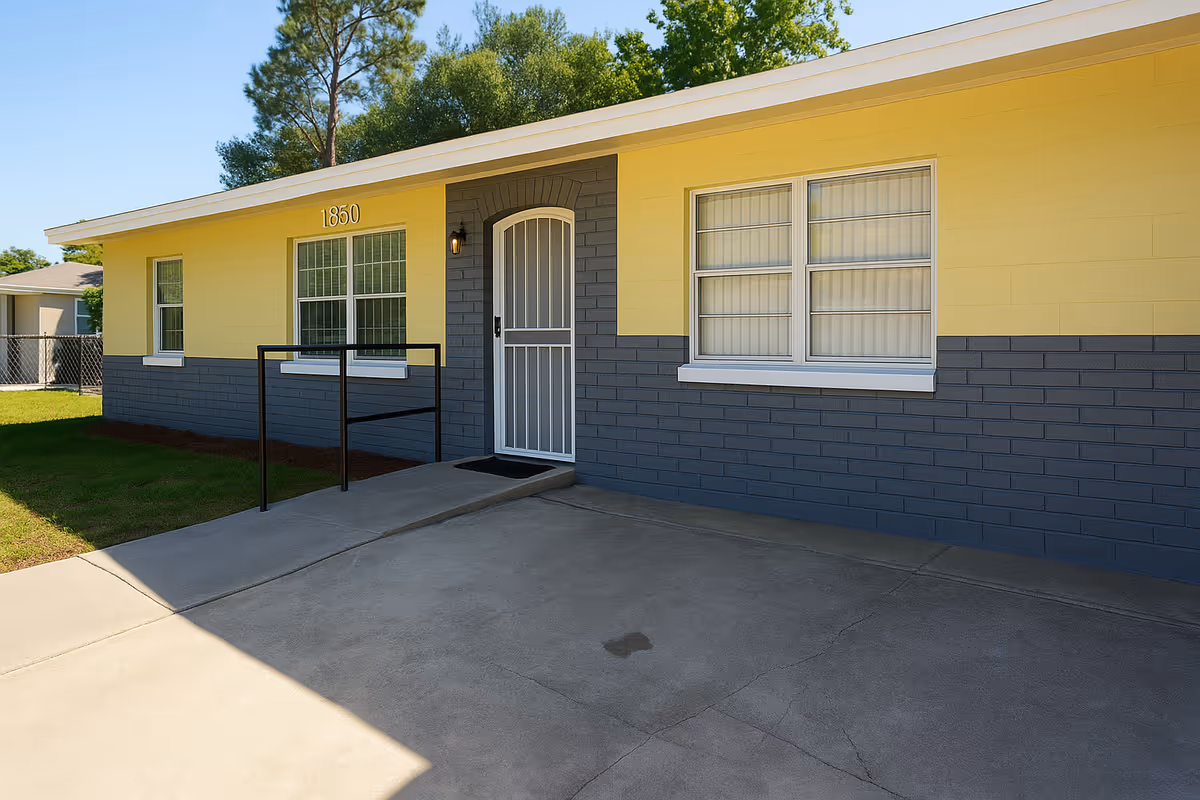 Front exterior of a single-story building with yellow and gray painted walls, a white security door, and the address number 1850.