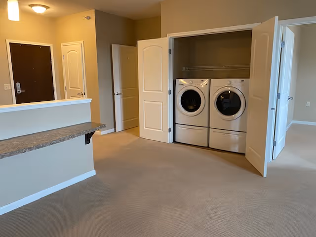 Interior room with an entryway, a countertop bar, and an open closet revealing a front-loading washer and dryer.