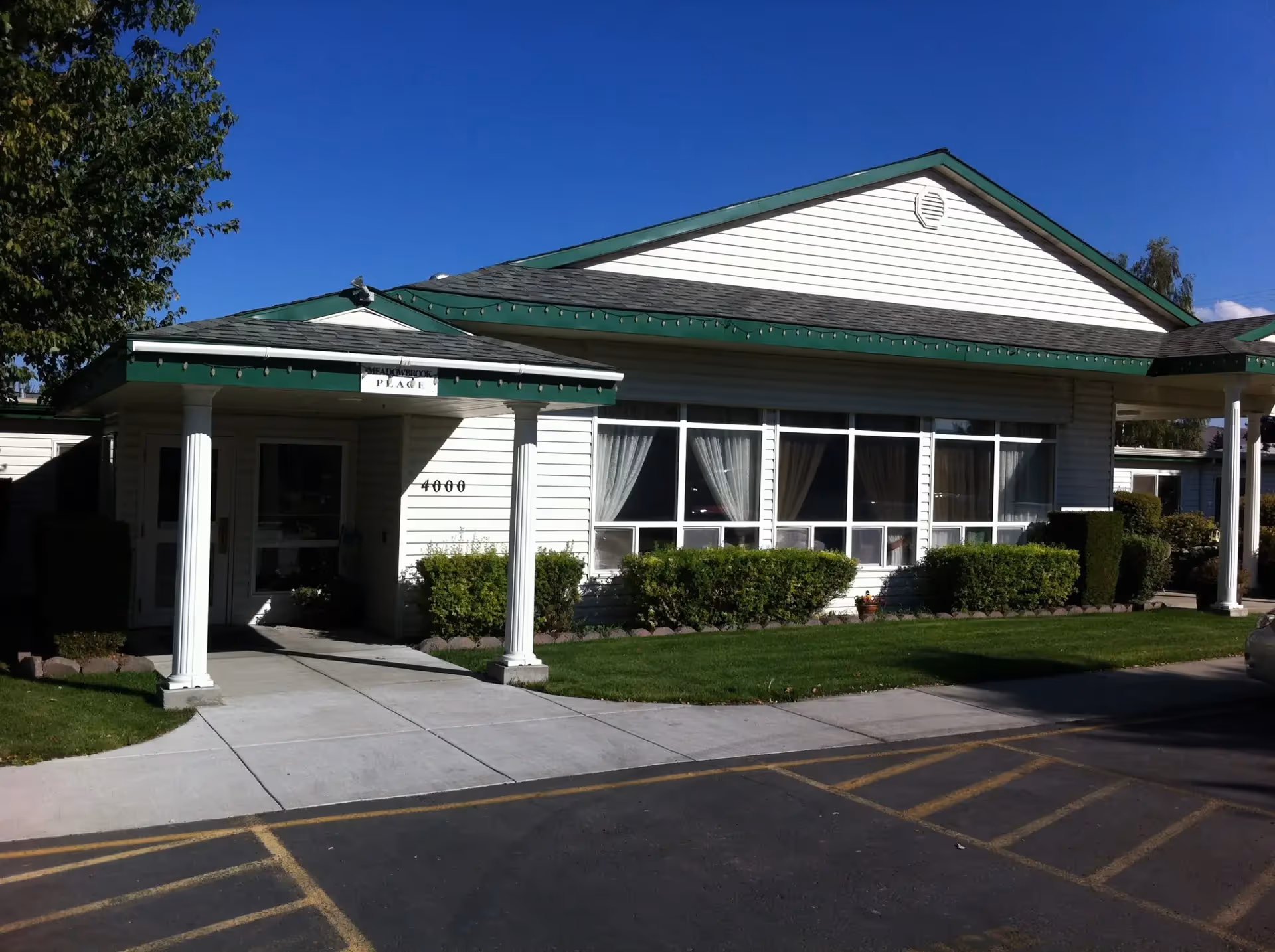 Front exterior of Meadowbrook Place Assisted Living building with entrance and shrubs.