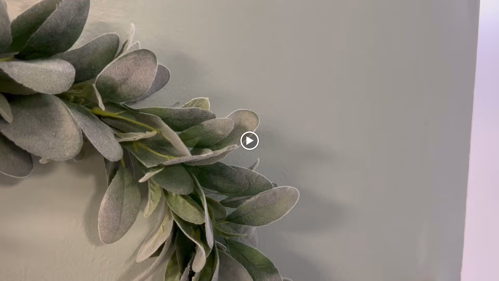 Close-up of a green leafy decorative wreath on a pale gray wall.
