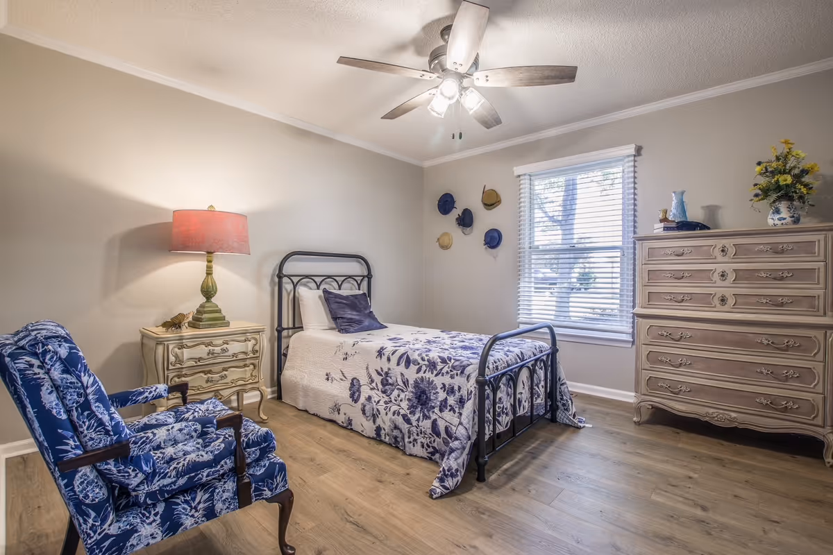 A cozy bedroom with a metal bed, dresser, lamp, ceiling fan, and blue accents.
