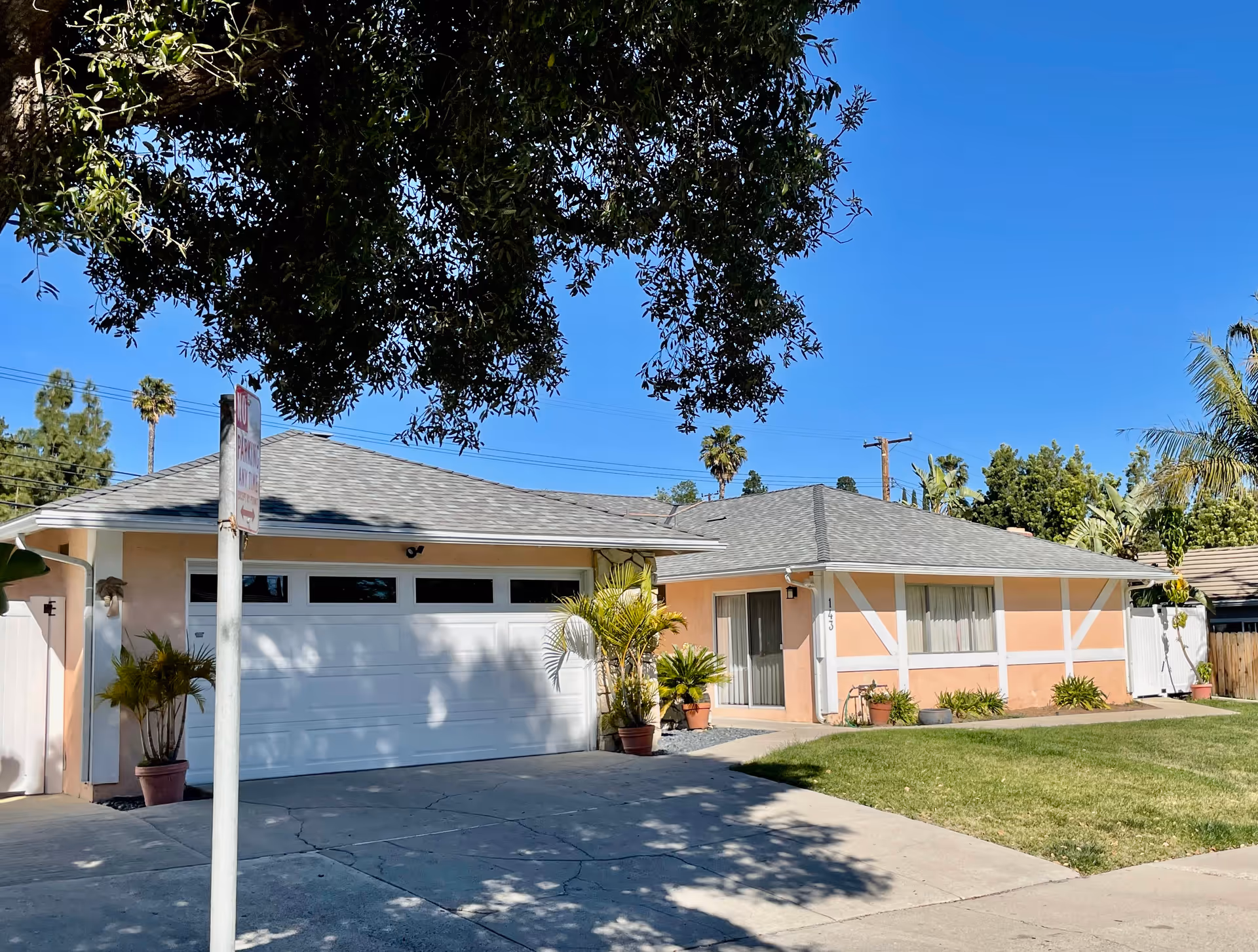Front view of a peach-colored single-story home with a two-car garage and palm trees.