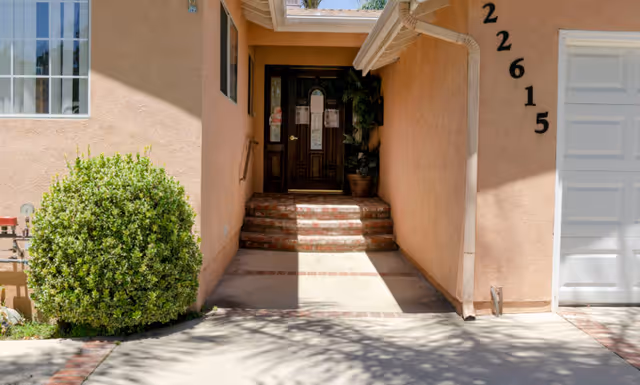 Exterior entrance to a peach-colored senior living facility with stairs leading to a dark wooden door.
