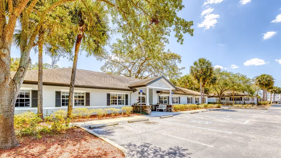 Front exterior of a single-story building with a covered entrance, palm trees and an empty parking lot.
