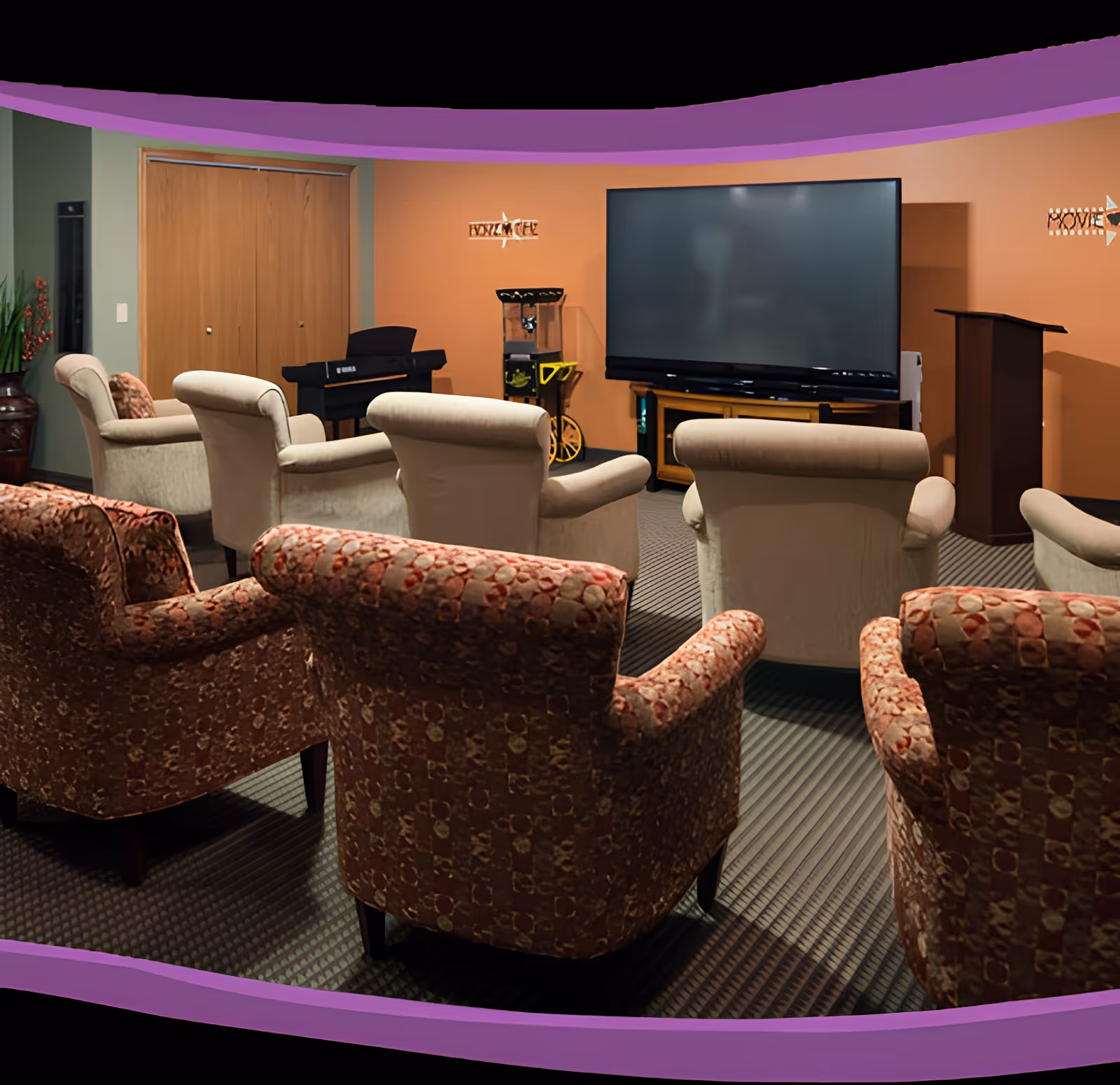 Seating area with rows of upholstered armchairs facing a large flat-screen TV and podium in a communal media room.