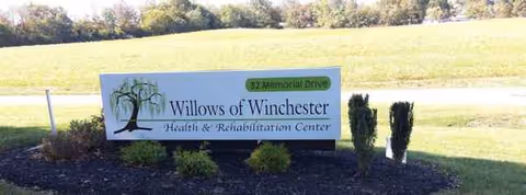 Outdoor sign for Willows of Winchester Health & Rehabilitation Center with manicured shrubs.