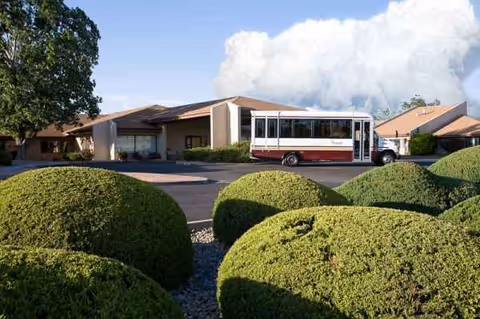 A single-story senior care facility with a red-and-white bus parked at the entrance.