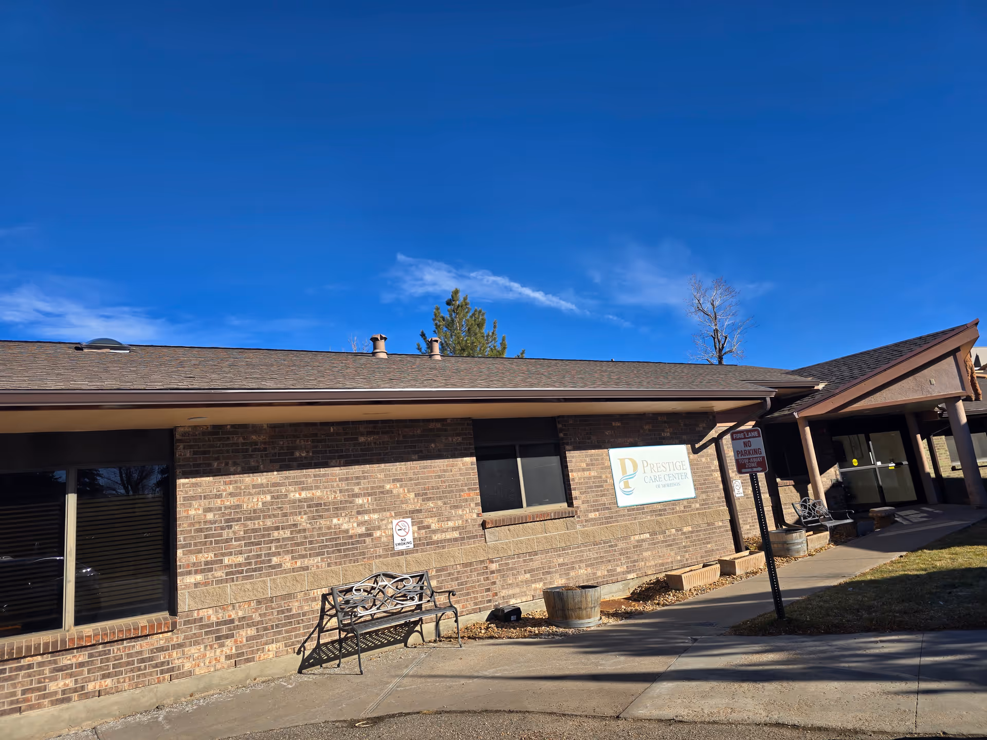Brick exterior front of Prestige Care Center of Morrison with benches, signage, and a clear blue sky.