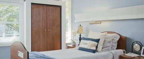 A neatly made bedroom in a senior living facility with a bed and wardrobe.
