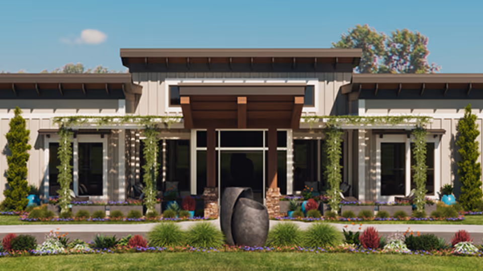 Front exterior view of a modern senior living facility building with a covered entrance, large windows, climbing plants on trellises, and landscaped garden with various shrubs and flowers in front.