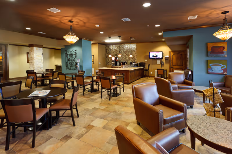 Spacious communal dining and lounge area with multiple tables, chairs, leather armchairs and a serving counter.