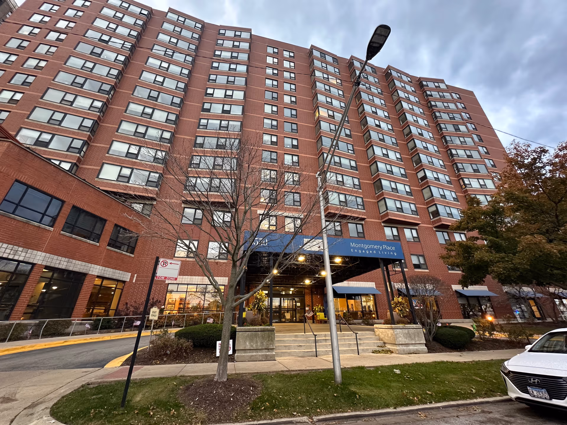 Front exterior of a tall red-brick building showing the Montgomery Place entrance canopy, steps, and sidewalk.