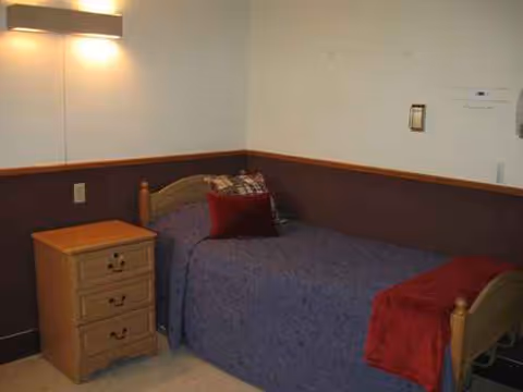 A small bedroom with a single bed, nightstand, blue bedspread, and red accents.