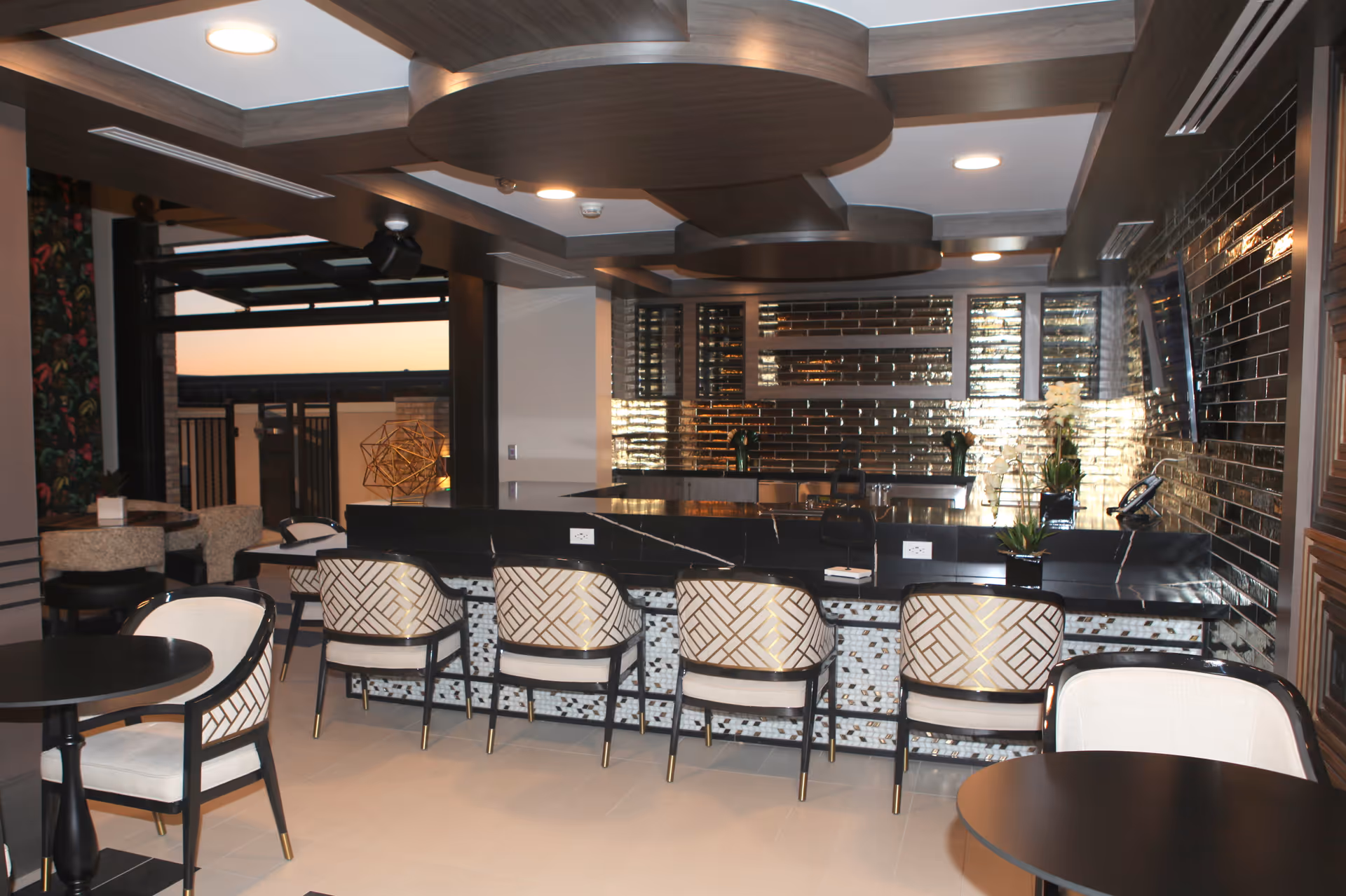 Modern indoor dining and bar area with a tiled bar counter, upholstered chairs, and decorative ceiling panels.
