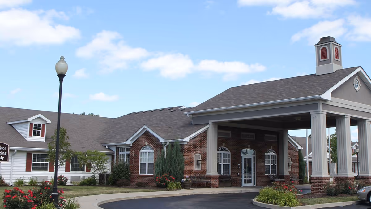 Front entrance of a brick-and-siding senior living building with a covered porte-cochère and landscaped driveway.