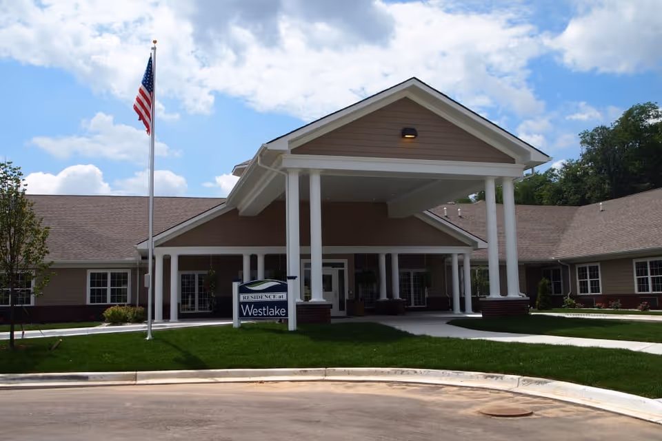 Front entrance of Westlake Health Campus with a covered portico, white columns, an American flag, and a Westlake sign.