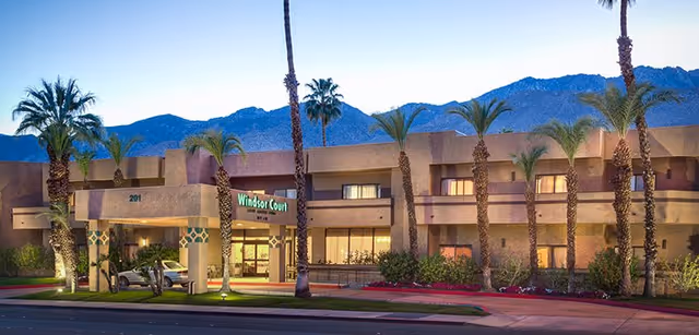Front exterior of Windsor Court Assisted Living at dusk with palm trees and an illuminated entrance.
