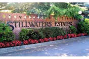Brick entrance sign for Stillwaters Estates surrounded by green shrubs and red flowers, with a palm tree in the background.