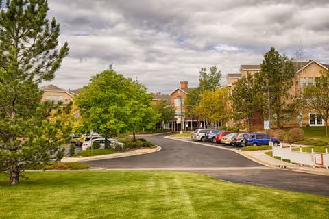 Exterior view of Someren Glen Retirement Community with lawn, trees, and parked cars.