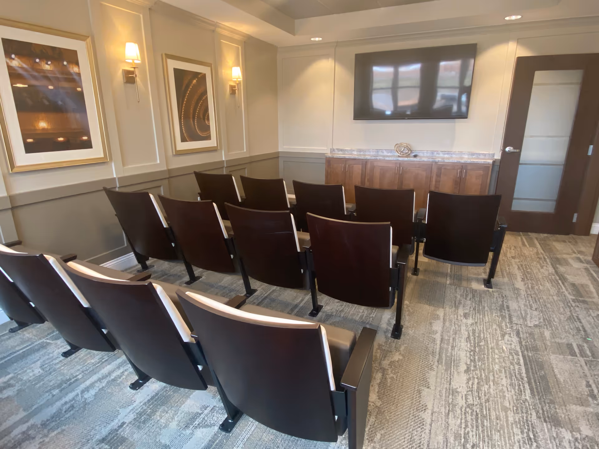 Rows of theater-style chairs facing a wall-mounted TV and cabinet in a small meeting/media room.