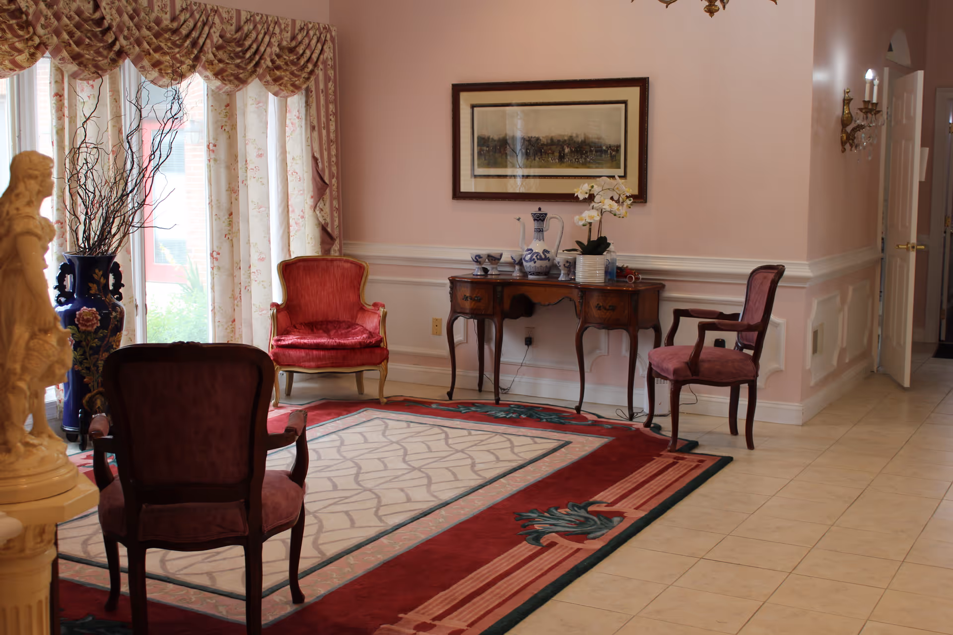 A formal sitting room with upholstered chairs around an area rug, a wooden console table with decorative vases, and floral curtains.