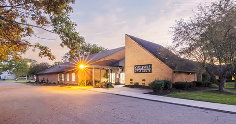 Brick single-story post-acute facility at dusk with a lit covered entrance, landscaping, and a sign reading 'Circleville Post Acute'.
