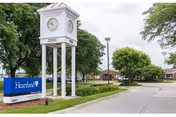 Exterior view with a white clock tower beside a sign along a tree-lined street.