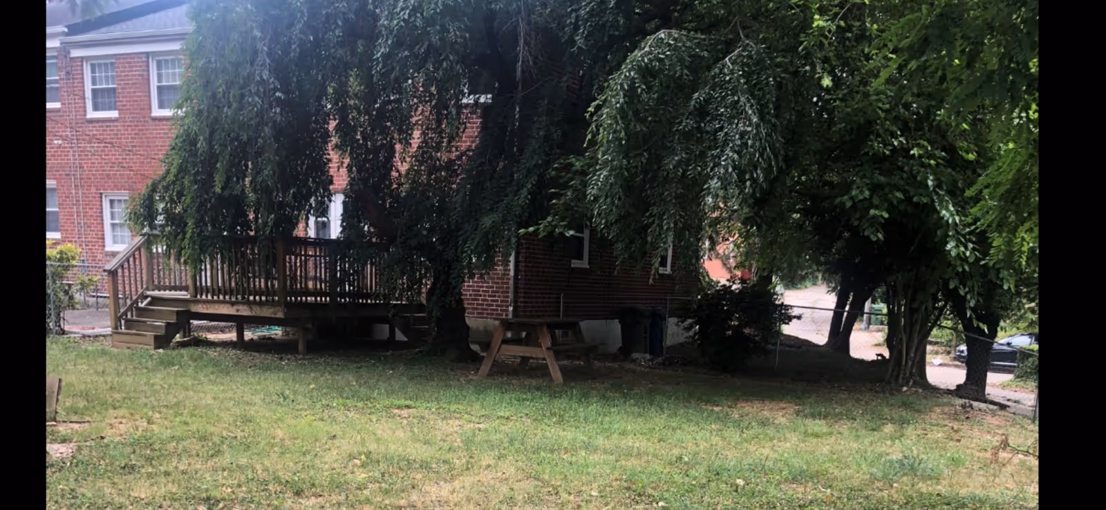 Brick building with a wooden deck, trees, and a grassy yard.