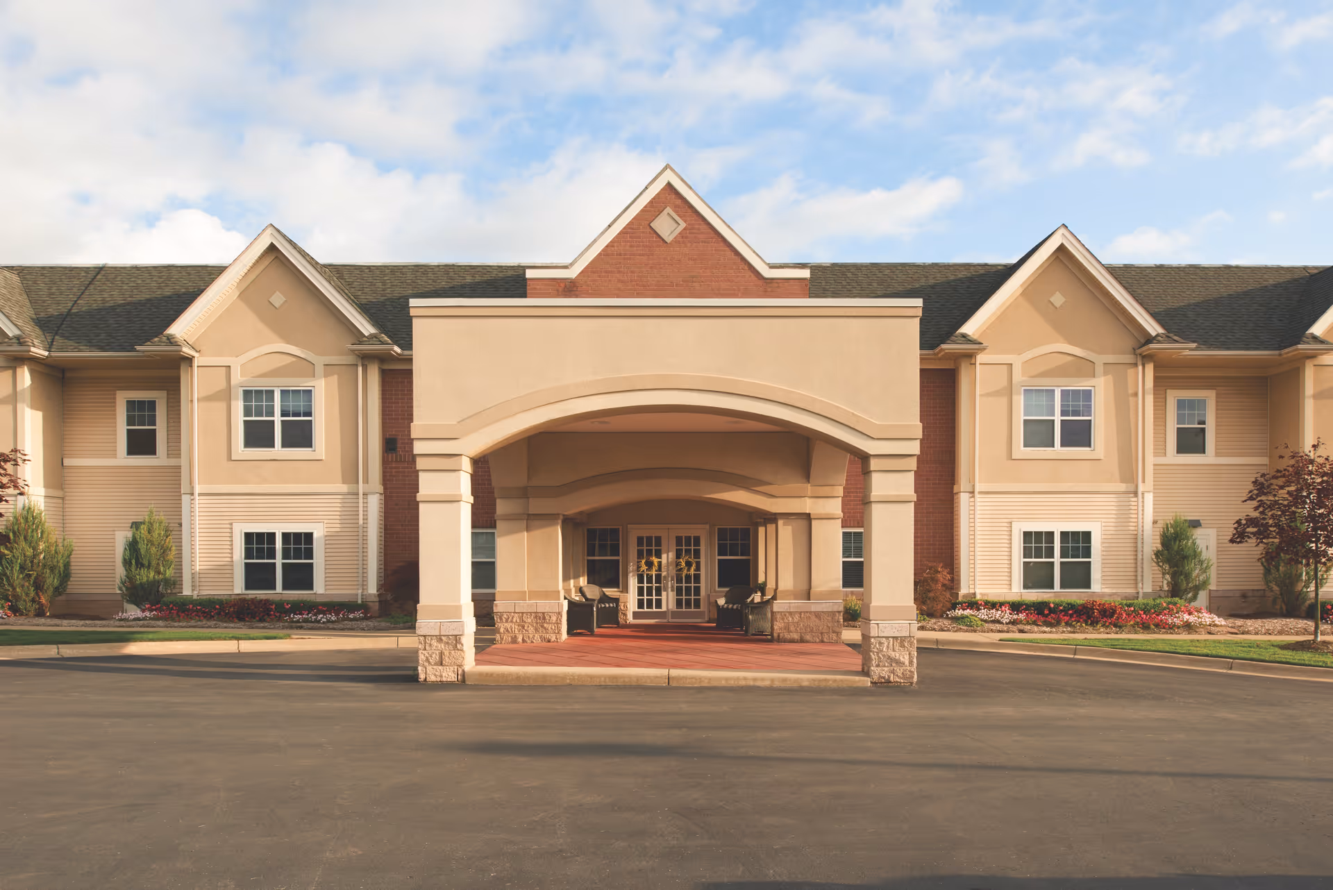 Front entrance of a two-story senior living building with a covered porte-cochère and symmetrical windows.