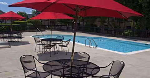 Outdoor pool area with red umbrellas and metal tables and chairs around the pool.