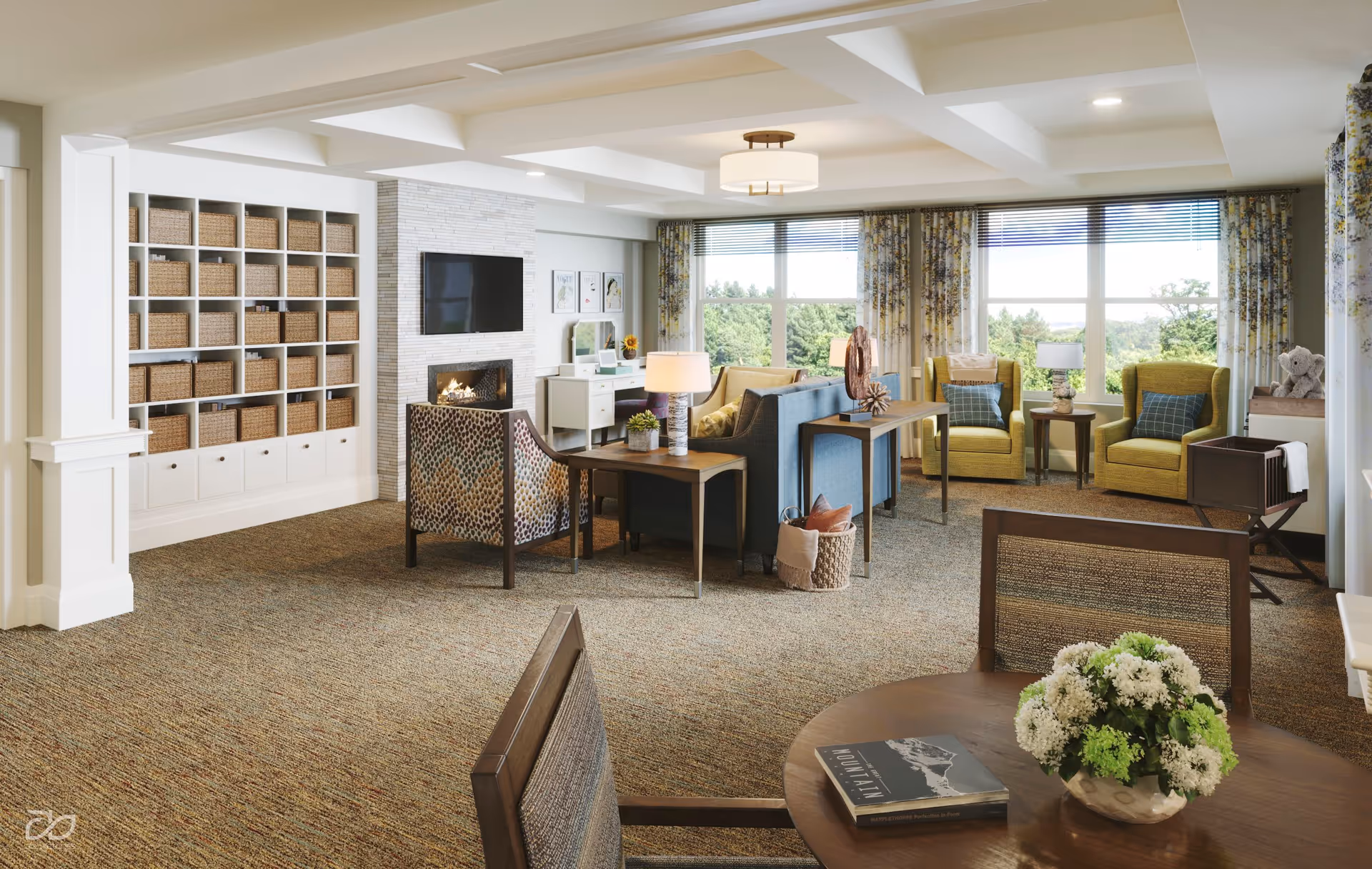 A bright and spacious living room area in a senior living facility featuring a cozy fireplace with a mounted TV above it, a wall of cubby shelves filled with wicker baskets, multiple seating arrangements including blue sofas, patterned armchairs, and green armchairs near large windows with floral curtains. A round wooden table with a flower arrangement and a book is in the foreground. The room has carpeted floors and recessed lighting.