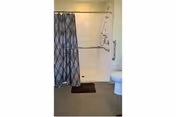 A bathroom with a shower area enclosed by a patterned shower curtain, a white toilet, and a grab bar on the wall next to the shower.