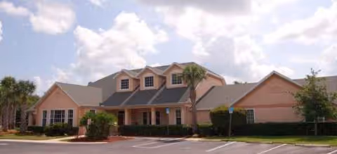 Exterior view of a peach-colored senior living facility with palm trees and a parking lot.