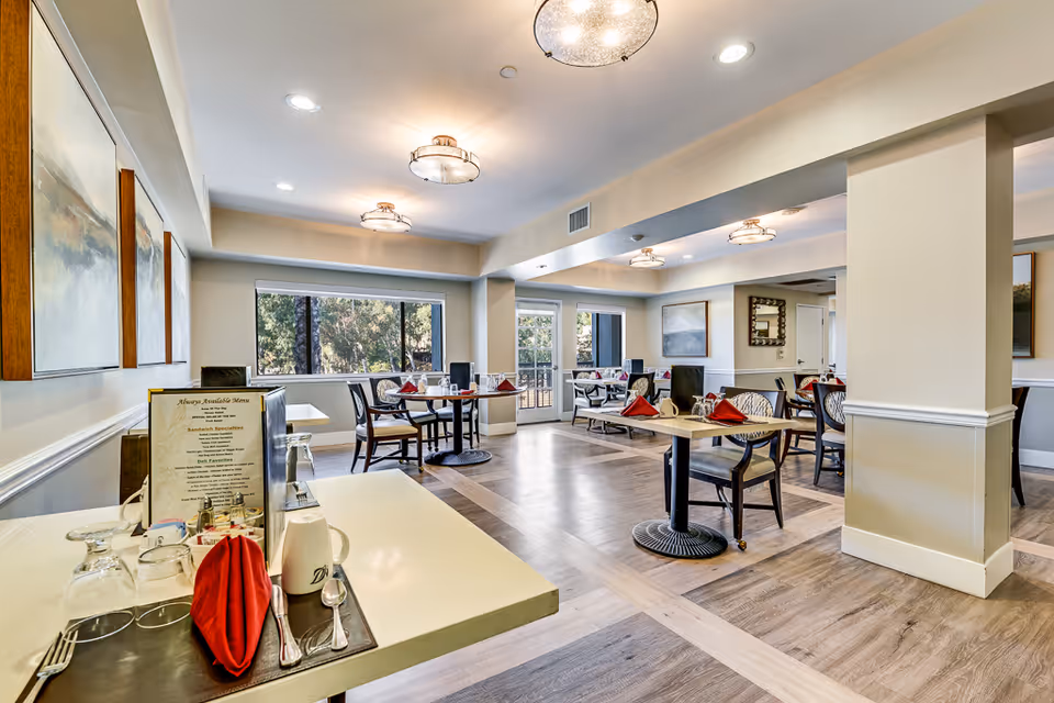 Bright communal dining room with multiple set tables, large windows, and modern ceiling lights.