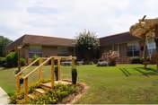Front exterior of a single-story brick nursing center with a green lawn and wooden ramp.