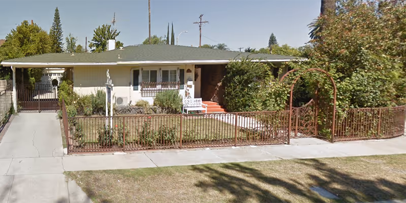 Single-story ranch-style house with a gated front yard, driveway, and arched metal trellis at the entrance.