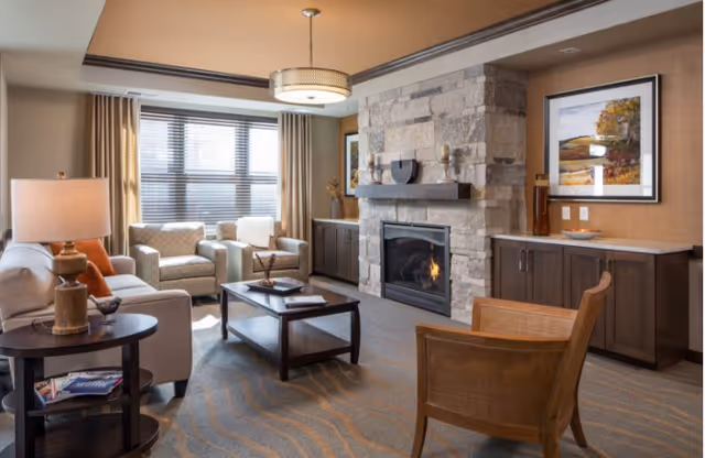 Sunlit communal living room with sofas and armchairs arranged around a coffee table and a stone fireplace with built-in cabinetry.