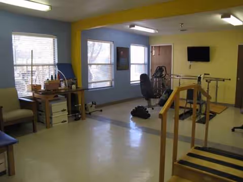 Bright interior gym in a senior facility with exercise machines, free weights, and a TV.